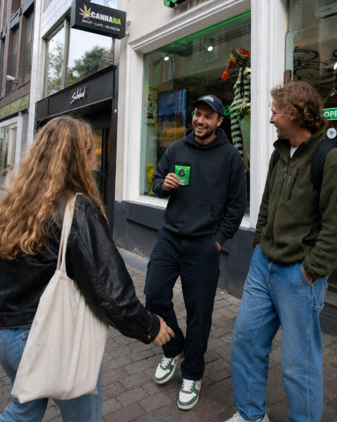zwei junge Männer und eine Frau lachen vor dem Laden CANNANA und halten CBD Blütentütchen in der Hand