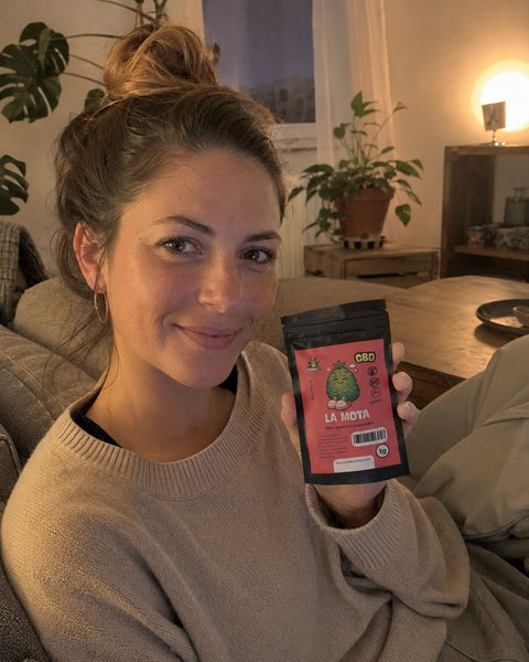 Frau sitzt auf einem Sofa und hält ein CBD-Blütentütchen in einem gemütlichen Wohnzimmer