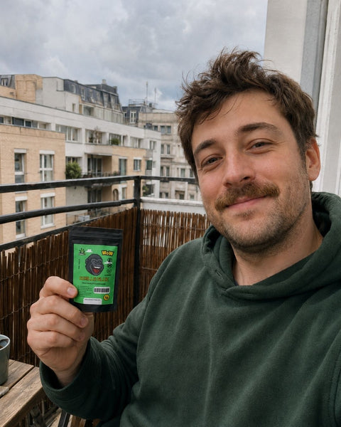 Erwachsener Mann hält ein CBD-Blütentütchen auf einem kleinen Stadtbalkon in der Hand